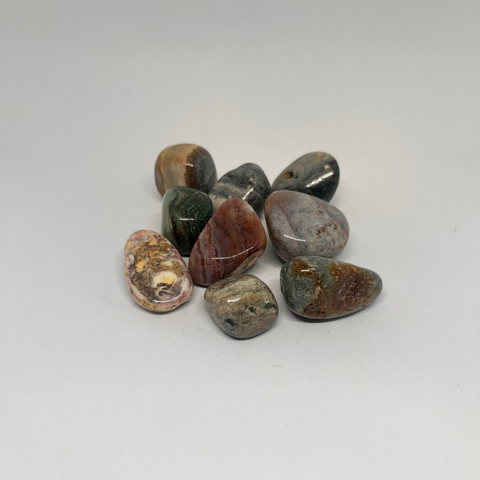 Ocean Jasper Tumbled Stones in a variety of warm colors, including greens, reds, and yellows, with distinct circular patterns and smooth, polished surfaces showcasing the stone's natural beauty.
