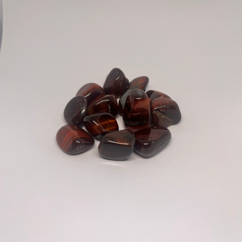 Red Tiger Eye Tumbled Stones with a glossy, polished finish showcasing rich red and brown bands, known for their grounding energy, ability to boost confidence, and promote vitality and focus.
