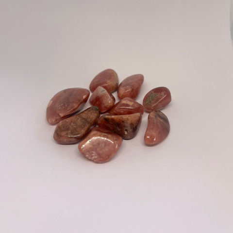 Rhodochrosite Tumbled Stones displaying smooth, polished crystals in soft pink and red hues with natural patterns, known for their heart-healing properties and ability to promote self-love and emotional growth.