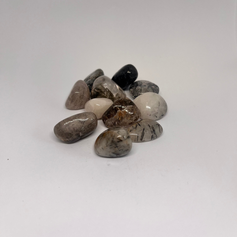 Tourmalinated Quartz Tumbled Stones with clear quartz showcasing embedded black tourmaline inclusions, arranged in a scattered formation on a white background.