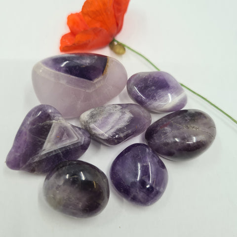 Chevron Amethyst Tumbled Stone showcasing smooth, polished crystals with banded purple hues, known for their ability to enhance insight, spiritual protection, and emotional healing.