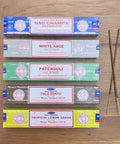 Satya Incense Best Seller Bundle showcasing Nag Champa Satya Incense, Satya White Sage, Satya Patchouli, Satya Palo Santo and Satya Tropical Lemongrass all laid flat on a wooden background.