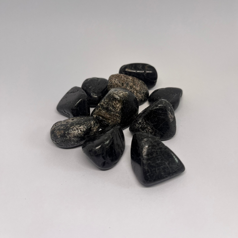 Black Tourmaline Tumbled Stones with glossy black surfaces and slight natural variations, arranged in a scattered formation on a white background.