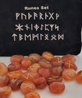 Carnelian rune stones with golden symbols scattered in front of a black pouch featuring runic designs, showcasing their smooth, polished surfaces and vibrant orange hues.