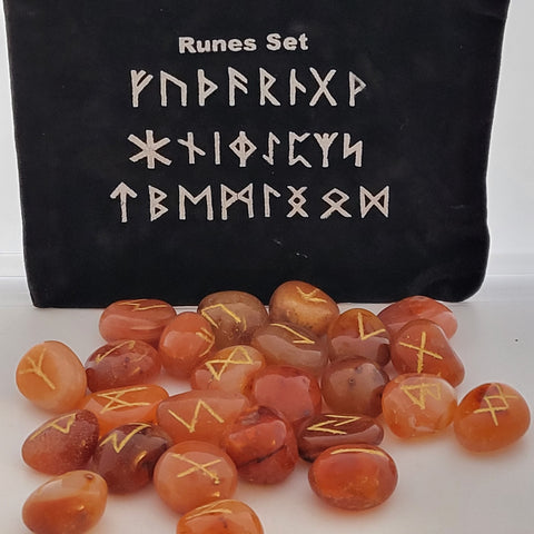 Carnelian rune stones with golden symbols scattered in front of a black pouch featuring runic designs, showcasing their smooth, polished surfaces and vibrant orange hues.