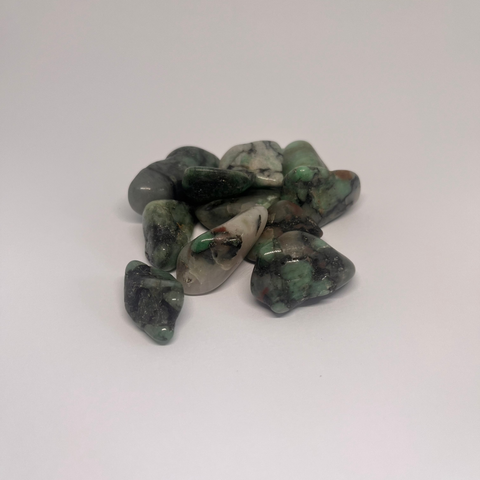 Emerald Tumbled Stones showcasing vibrant green hues with subtle veins of other colors, arranged in a group on a white background.