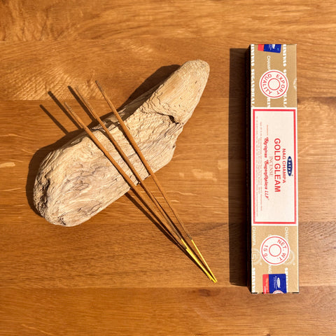Satya Gold Gleam Incense Sticks 15g box on a wooden background, designed to bring brightness and positive energy.