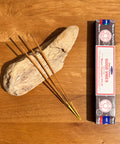 Satya Good Vibes Nag Champa Incense Sticks 15g box on a wooden background, offering a joyful and uplifting fragrance.