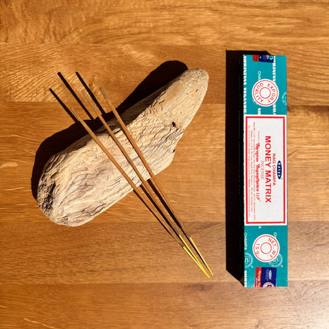 Satya Money Matrix Nag Champa Incense Sticks 15g box on a wooden background, designed to attract abundance.