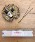 Satya Incense Protection Bundle showcasing White Sage Satya Incense, claro sage essential oil and a black obsidian crystal all laid flat on a wooden background.