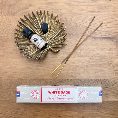 Satya Incense Protection Bundle showcasing White Sage Satya Incense, claro sage essential oil and a black obsidian crystal all laid flat on a wooden background.