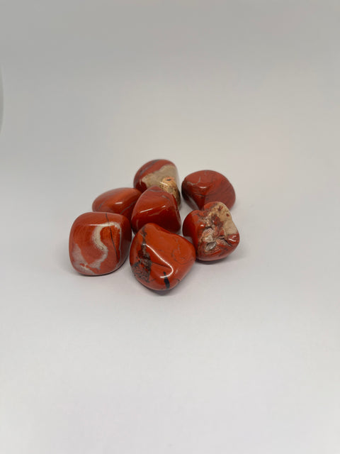 Red Jasper Tumbled Stones showcasing their smooth, polished surfaces with rich red hues and contrasting white and brown streaks, highlighting their natural beauty and vibrant color.