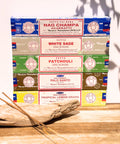 Satya Incense Best Seller Bundle showcasing Nag Champa Satya Incense, Satya White Sage, Satya Patchouli, Satya Palo Santo and Satya Tropical Lemongrass on a piece of driftwood with a white background.