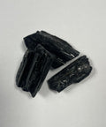 Three raw black tourmaline rough pieces on white background showing natural columnar crystal structure — Fragrant Heaven