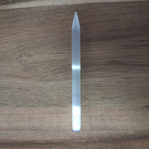 Slender selenite pointed wand on wooden background showing tapered tip and silky white surface — Fragrant Heaven
